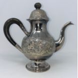 A white metal coffee pot with extensive embossed decoration, tests as silver