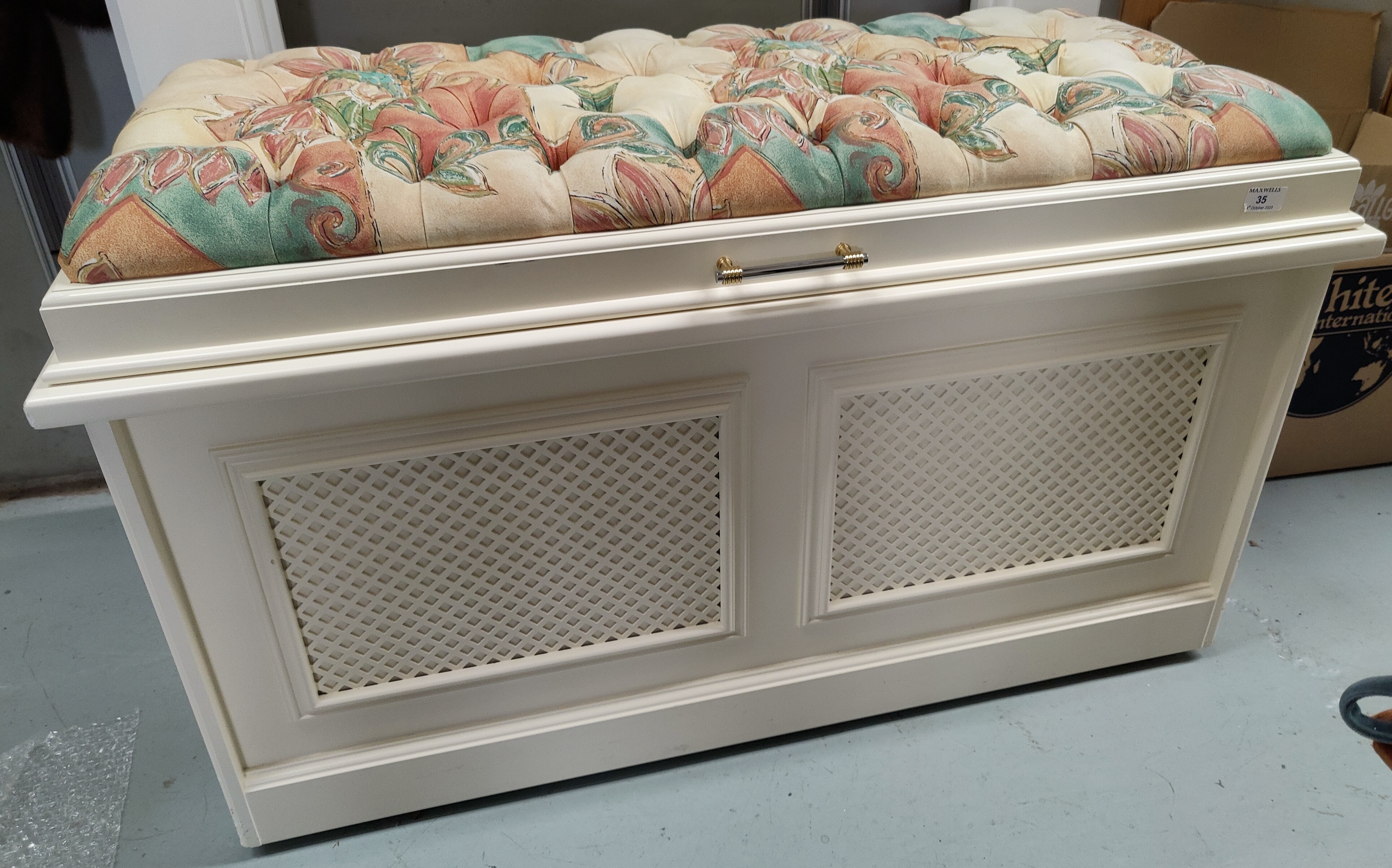 A modern cream painted ottoman with deeply buttoned patterned fabric top and lattice work front