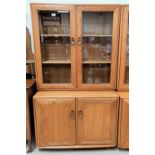 An Ercol light elm full height side cabinet with 2 shelves enclosed by glazed doors, cupboards