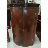 An 18th century crossbanded oak corner cupboard, the bow front enclosed by 2 doors