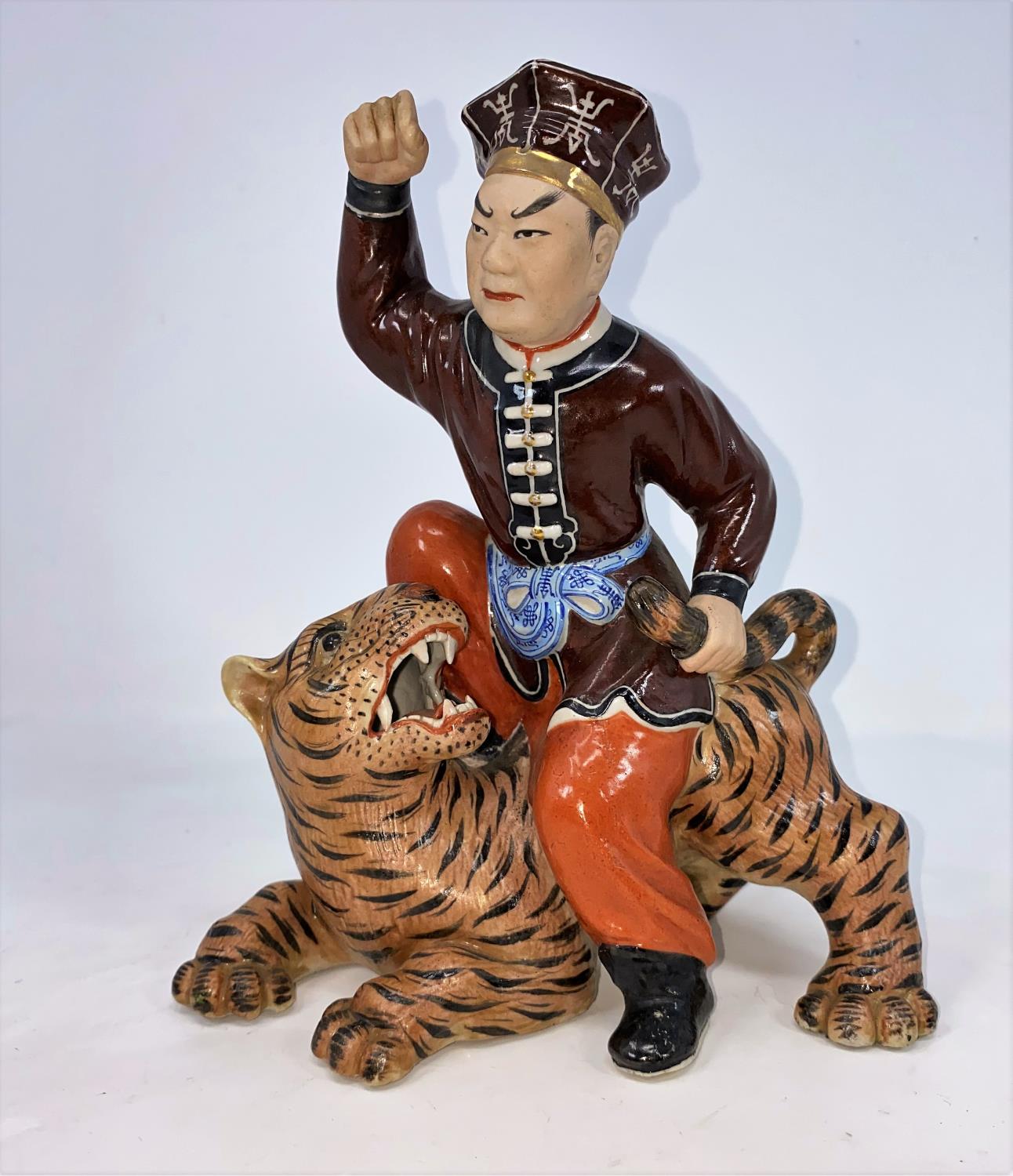 A Chinese ceramic figure of man seated on a tiger holding its tail, unmarked, height 21.5cm