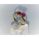 A yellow metal cross over style dress ring set with 2 ruby coloured stones, unmarked tests as 18 ct,