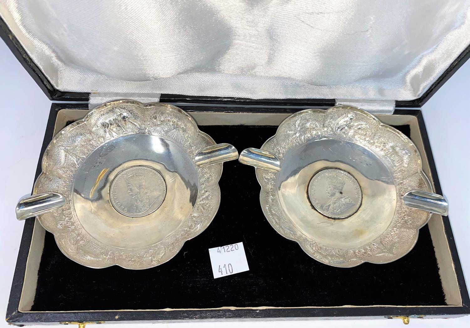 A cased pair of Indian white metal ash trays with scalloped and embossed borders, each inset with