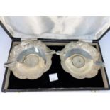 A cased pair of Indian white metal ash trays with scalloped and embossed borders, each inset with