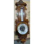 An Edwardian aneroid barometer with exposed mechanism, and thermometer, in carved golden oak case,