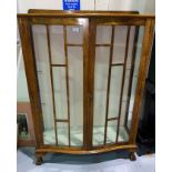 A 1930's golden oak display cabinet with serpentine front and 2 glazed doors, on ball and claw feet,