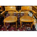 An Edwardian pair of golden oak office chairs, tub shaped with pierced rail backs and studded