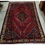 A mid 20th century Persian rug with red ground, geometric stylised floral motifs, central barred