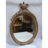 An early 19th century carved giltwood looking glass with urn and harebell surmount, the oval (
