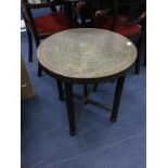 AN EASTERN BRASS CIRCULAR TABLE WITH FOLDING WOODEN SUPPORTS