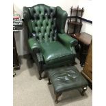 A GREEN LEATHER WING BACK ARMCHAIR AND MATCHING FOOTSTOOL