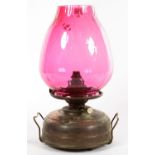 AN OXIDISED BRASS OIL LAMP WITH A DIMPLED CRANBERRY GLASS SHADE, 44CM H, ADAPTED FOR ELECTRICITY