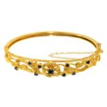 A SAPPHIRE SET 9CT GOLD BANGLE, OF OPENWORK FLORAL DESIGN WITH PLAIN LOWER HALF, 13G