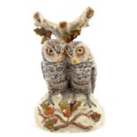 A CONTINENTAL PORCELAIN GROUP OF TWO GLASS EYED OWLS PERCHED ON A RUSTIC MOUND, APPLIED WITH OAK