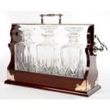 AN EPNS MOUNTED MAHOGANY TANTALUS AND SET OF THREE GLASS DECANTERS AND STOPPERS, 32CM H