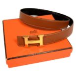 HERMÉS. REVERSIBLE 'H' BELT. TAN LEATHER / BLACK STRAP WITH GOLD PLATED BUCKLE. 98 CM L, BOXED