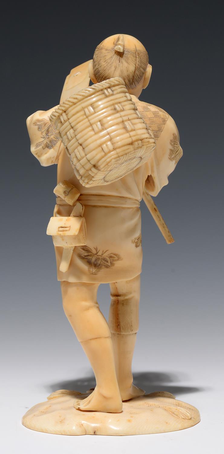 A JAPANESE SECTIONAL IVORY FIGURE OF A FARMER CARRYING A BASKET OVER HIS SHOULDER AND HOLDING A - Image 2 of 2