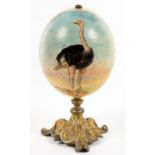 A LATE 19TH C PAINTED OSTRICH EGG ON ORNATE CAST GILT BRASS FOOT, 21CM H