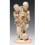 A JAPANESE IVORY OKIMONO OF A STREET VENDOR AND HIS SMALL SON, THE MAN'S FOOT RESTING ON A