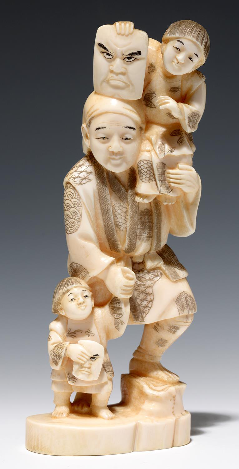 A JAPANESE IVORY OKIMONO OF A MASK SELLER AND TWO CHILDREN, 17CM H, SIGNED, MEIJI PERIOD