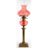 A BRASS COLUMNAR OIL LAMP WITH CRANBERRY GLASS FOUNT AND BRASS BURNER, CONFORMING SHADE, 73CM H