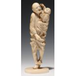 A JAPANESE IVORY OKIMONO OF A MAN CARRYING HIS YOUNG SON ON HIS LEFT ARM, 15CM H, SIGNED