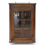 A SPLAY FRONTED OAK HANGING CORNER CABINET WITH NULLED FRIEZE AND SIX PLAIN DOORS WITH SERPENT