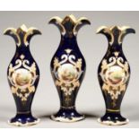 A SAMUEL ALCOCK COBALT GROUND GARNITURE OF THREE VASES, OF SLENDER FORM, PAINTED WITH A VIGNETTE