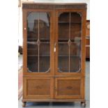 AN OAK BOOKCASE WITH CARVED FRIEZE, FITTED WITH ADJUSTABLE SHELVES ENCLOSED BY GLAZED DOORS, THE