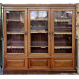 AN EDWARDIAN WALNUT BOOKCASE, FITTED WITH ADJUSTABLE SHELVES AND ENCLOSED BY THREE GLAZED DOORS, THE