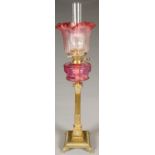 AN EDWARDIAN BRASS COLUMNAR OIL LAMP, WITH CRANBERRY GLASS FOUNT, BRASS BURNER AND STOP FLUTED