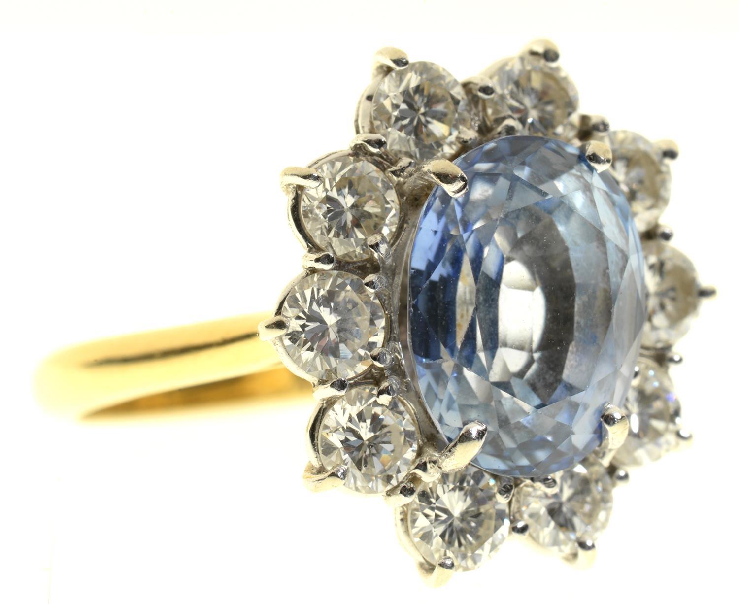 A CORNFLOWER SAPPHIRE AND DIAMOND RING  the oval sapphire in a surround of ten evenly sized round - Image 2 of 6