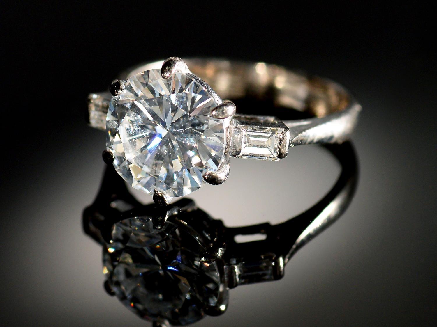 A DIAMOND  RING   the round brilliant cut diamond of approx 3.2cts flanked by a baguette diamond