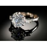 A DIAMOND  RING   the round brilliant cut diamond of approx 3.2cts flanked by a baguette diamond