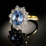A CORNFLOWER SAPPHIRE AND DIAMOND RING  the oval sapphire in a surround of ten evenly sized round