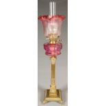 AN EDWARDIAN BRASS COLUMNAR OIL LAMP, WITH CRANBERRY GLASS FOUNT, BRASS BURNER ON STOP FLUTED