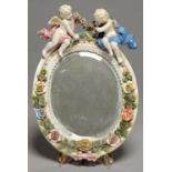 A SITZENDORF FLORAL ENCRUSTED OVAL MIRROR, LATE 19TH C, SURMOUNTED BY TWO PUTTI, 30CM H,