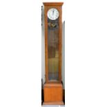 AN OAK LONGCASE ELECTRIC TIMEPIECE, EARLY 20TH C WITH GLAZED DOOR, THE BASE WITH DOOR TO THE BATTERY