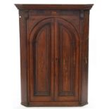 A GEORGE III INLAID OAK CORNER CUPBOARD WITH PANELLED ARCH DOORS WITH LION PATERAE, 135CM H; 101 X
