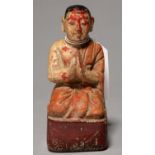 A SOUTH EAST ASIAN POLYCHROME WOOD SCULPTURE OF A KNEELING DEVOTEE, ON OBLONG RED BASE, 14CM H Paint