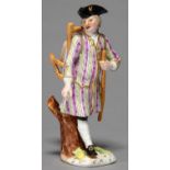 A GERMAN FIGURE OF A PEDLAR, 19TH C, CARRYING A PACK IN A SCARF, IN PUCE AND GREEN STRIPED COAT