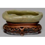 A CHINESE CELADON JADE BRUSH WASHER, 20TH C, CARVED AS A LOTUS, 12.5CM L, WOOD STAND (2) Tiny flea