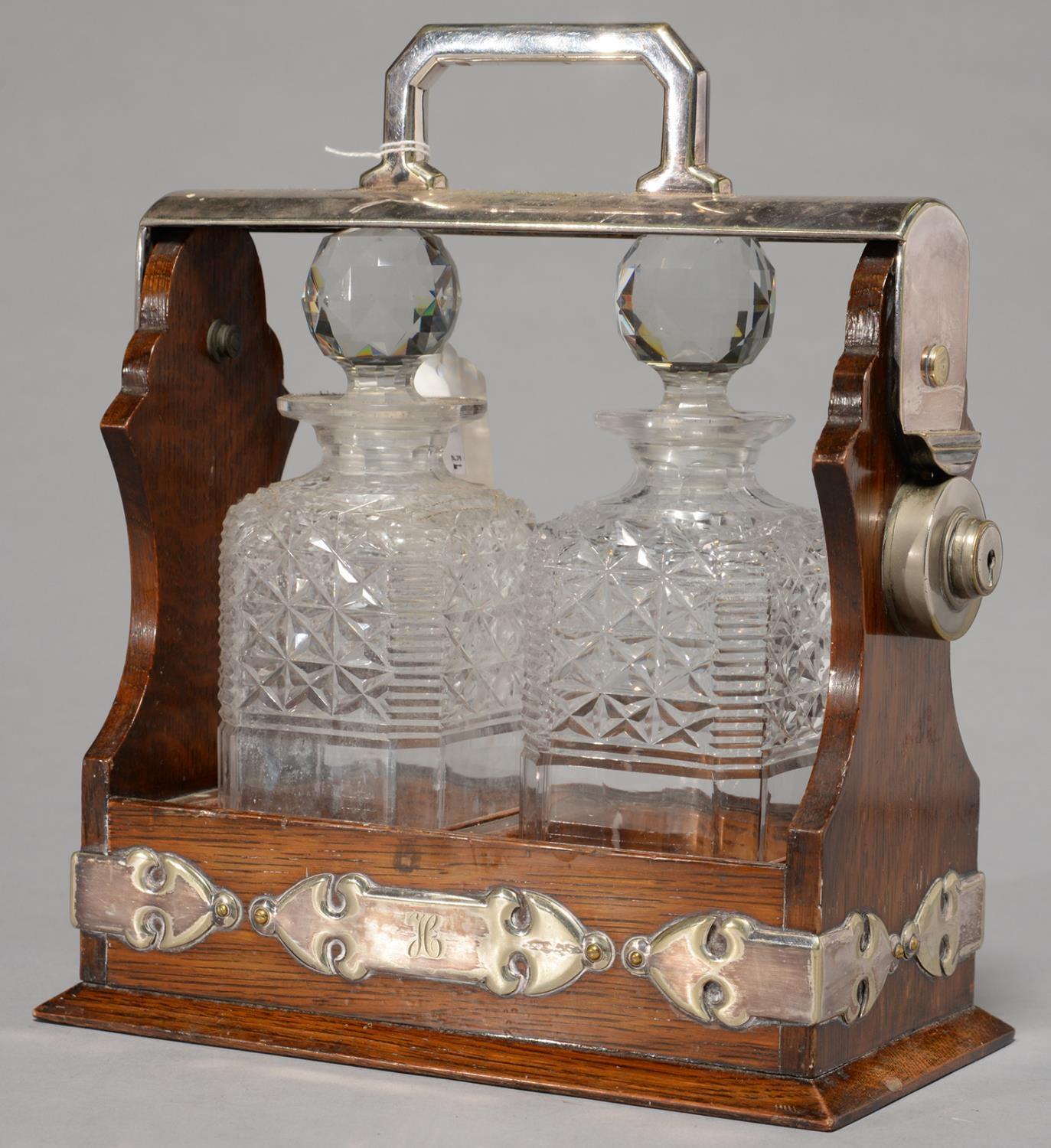 AN EDWARDIAN EPNS MOUNTED OAK TANTALUS, C1905, WITH PAIR OF CUT GLASS DECANTERS AND STOPPERS, 30CM H