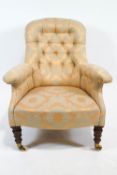 A Victorian button-back armchair on turned tapering mahogany legs with brass casters,
