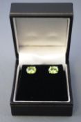 A white metal pair of single stone stud earrings. Each set with an oval faceted cut peridot.