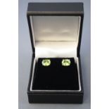 A white metal pair of single stone stud earrings. Each set with an oval faceted cut peridot.