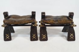 A pair of camel stools, each with leather seats,