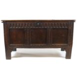 A 17th century oak coffer, the triple panelled front with carved frieze, uprights and apron,