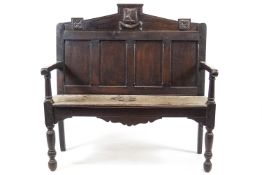 An oak hall bench with carved armorial on the cresting above a quadrupled panelled back