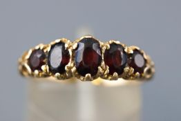 A yellow metal half hoop ring. Set with five graduated faceted cut garnets.